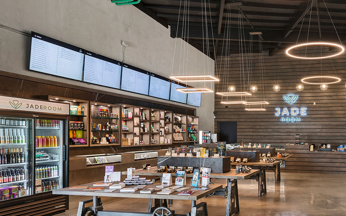 Wall of TVs above product shelving at Jaderoom dispensary